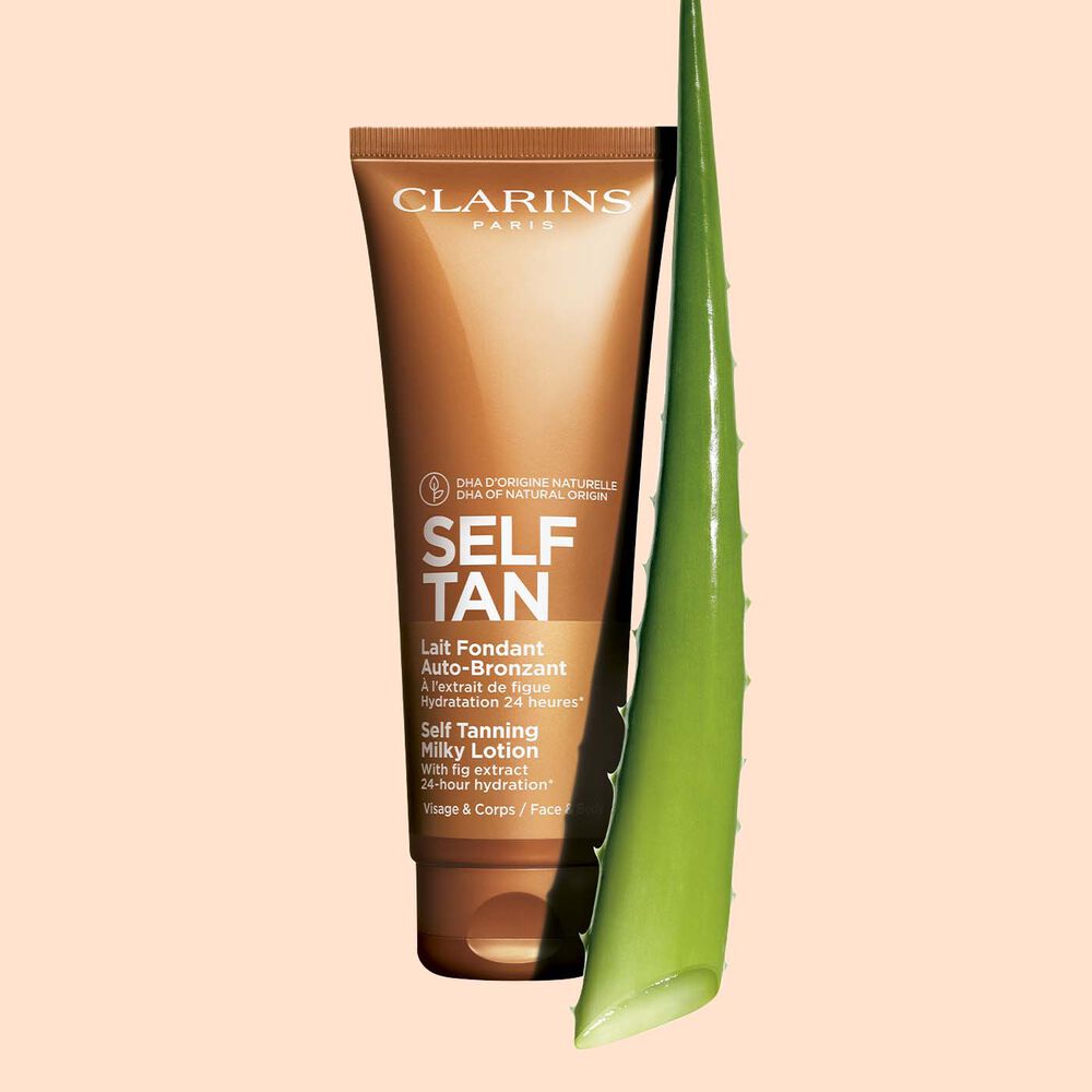 A tube of Clarins Self Tanning Milky Lotion close to a piece of aloe vera on a pale orange background.