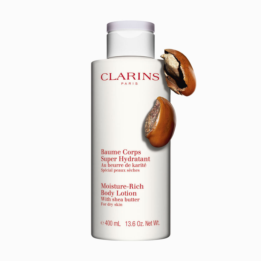 Bottle of Clarins Moisture-Rich Body Lotion close to some shea nuts on a white background.