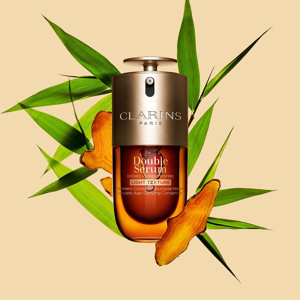 A 30 ml bottle of Clarins Double Serum Light Texture among turmeric and Provençal reed leaves against an orange background.