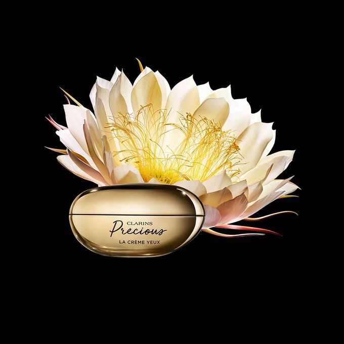Packshot of Clarins Precious Eyes eye cream close to a Moonlight flower on dark background.