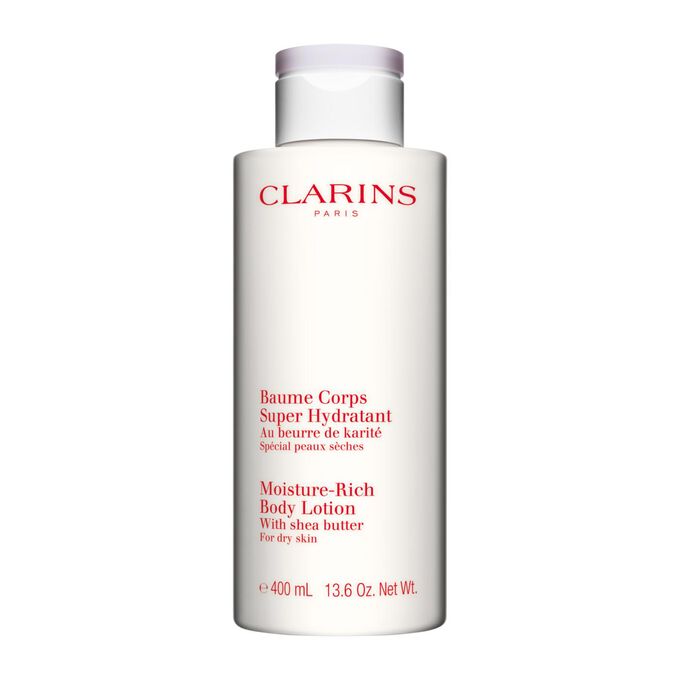 Bottle of Clarins Moisture-Rich Body Lotion close to some shea nuts on a white background.