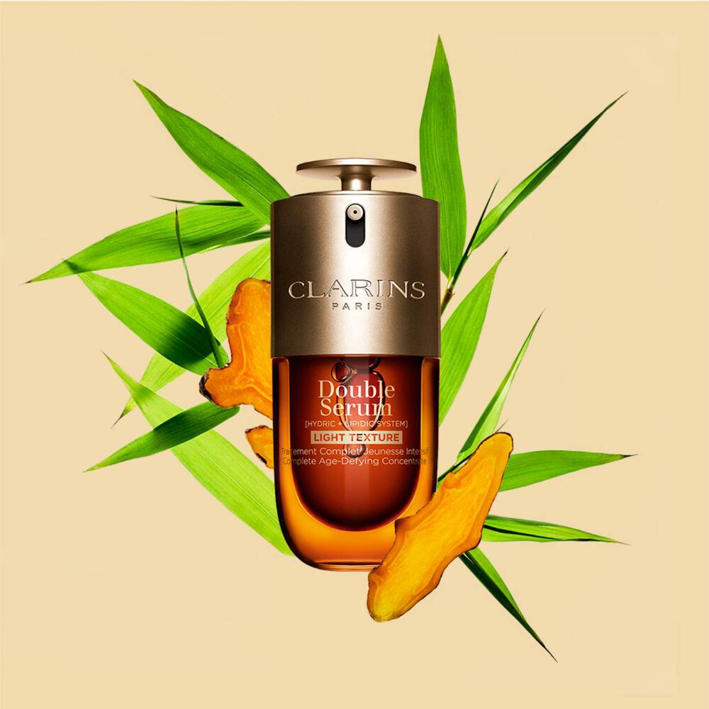 A 30 ml bottle of Clarins Double Serum Light Texture among turmeric and Provençal reed leaves against an orange background.