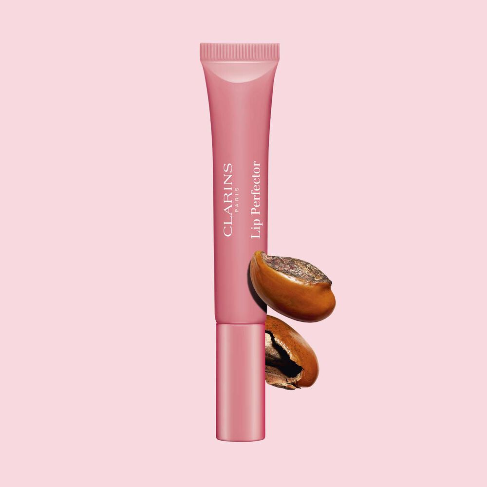 Packshot of Clarins Lip Perfector 01 Rose Shimmer repairing lip balm in front of a shea nuts on a pink background.