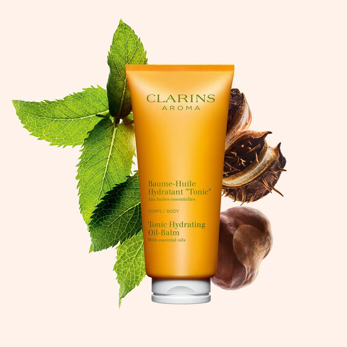 Packshot of a tube of Clarins Tonic Hydrating Oil-balm, close to some mint leaves and shea nuts on a peach background.