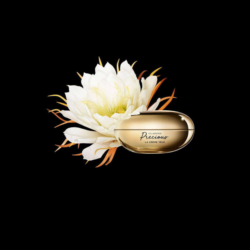 Packshot of Clarins Precious Eyes eye cream close to a Moonlight flower on dark background.