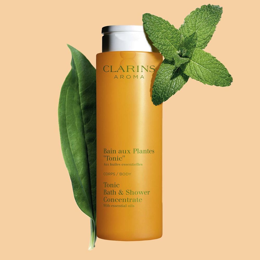Packshot of Clarins Tonic Bath and Shower Concentrate gel, close to some mint and rosemary leaves on an orange background.