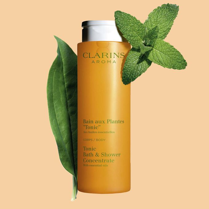 Packshot of Clarins Tonic Bath and Shower Concentrate gel, close to some mint and rosemary leaves on an orange background.