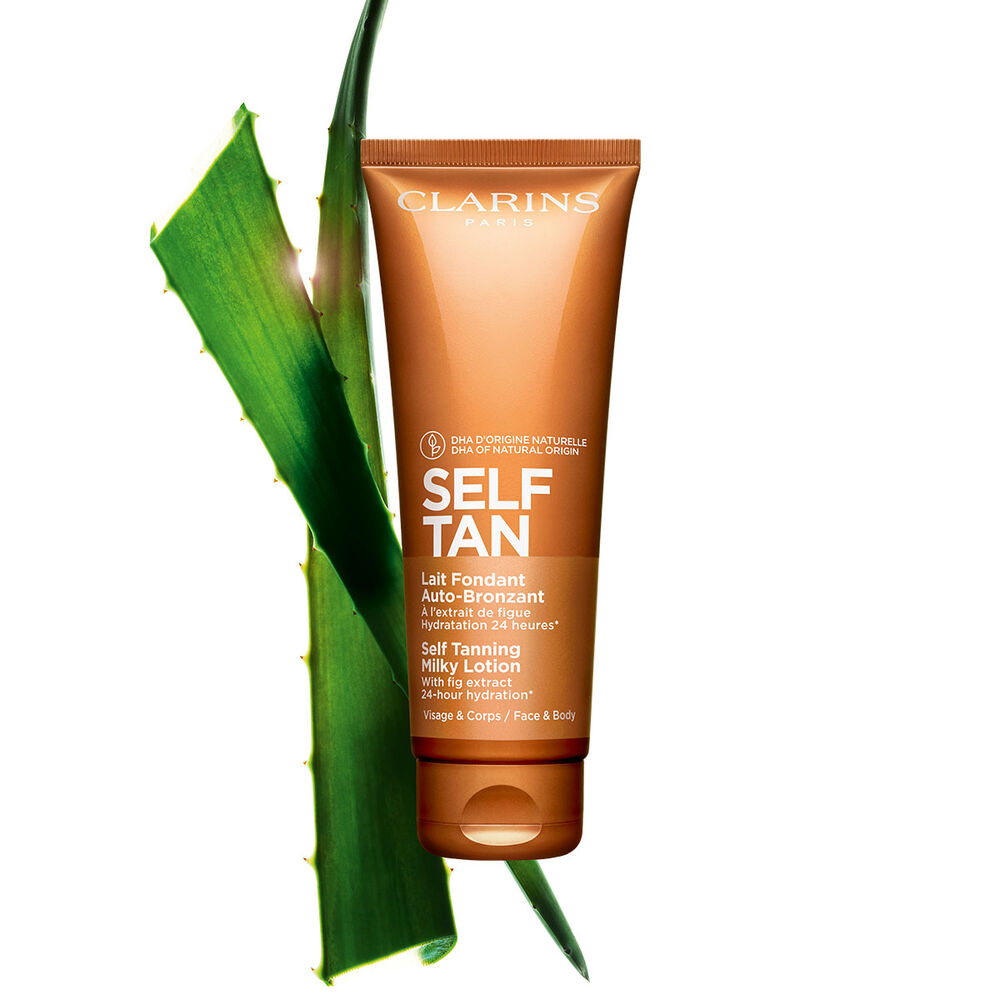 A tube of Clarins Self Tanning Milky Lotion close to a piece of aloe vera on a pale orange background.