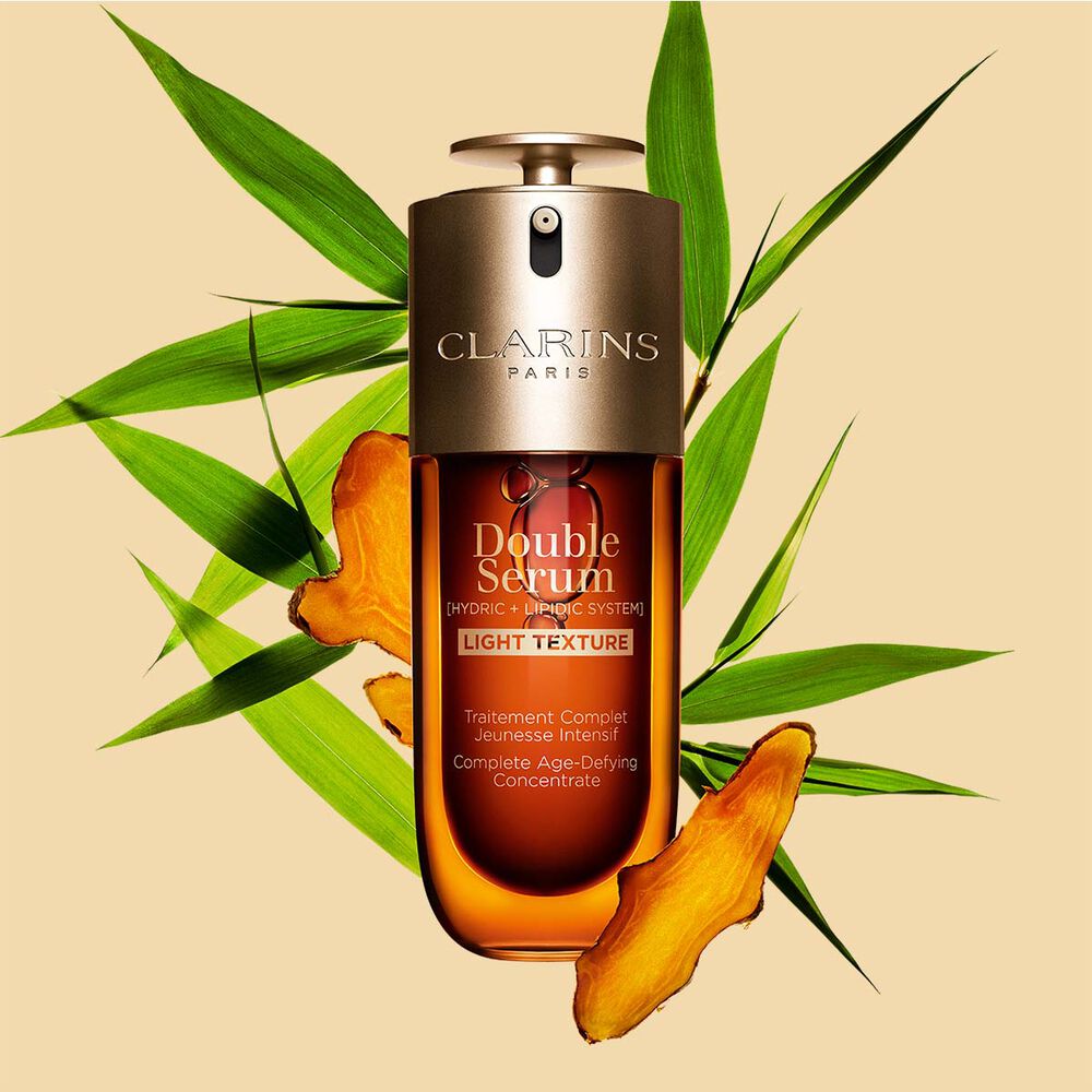 A 50 ml bottle of Clarins Double Serum Light Texture among turmeric and Provençal reed leaves against an orange background.