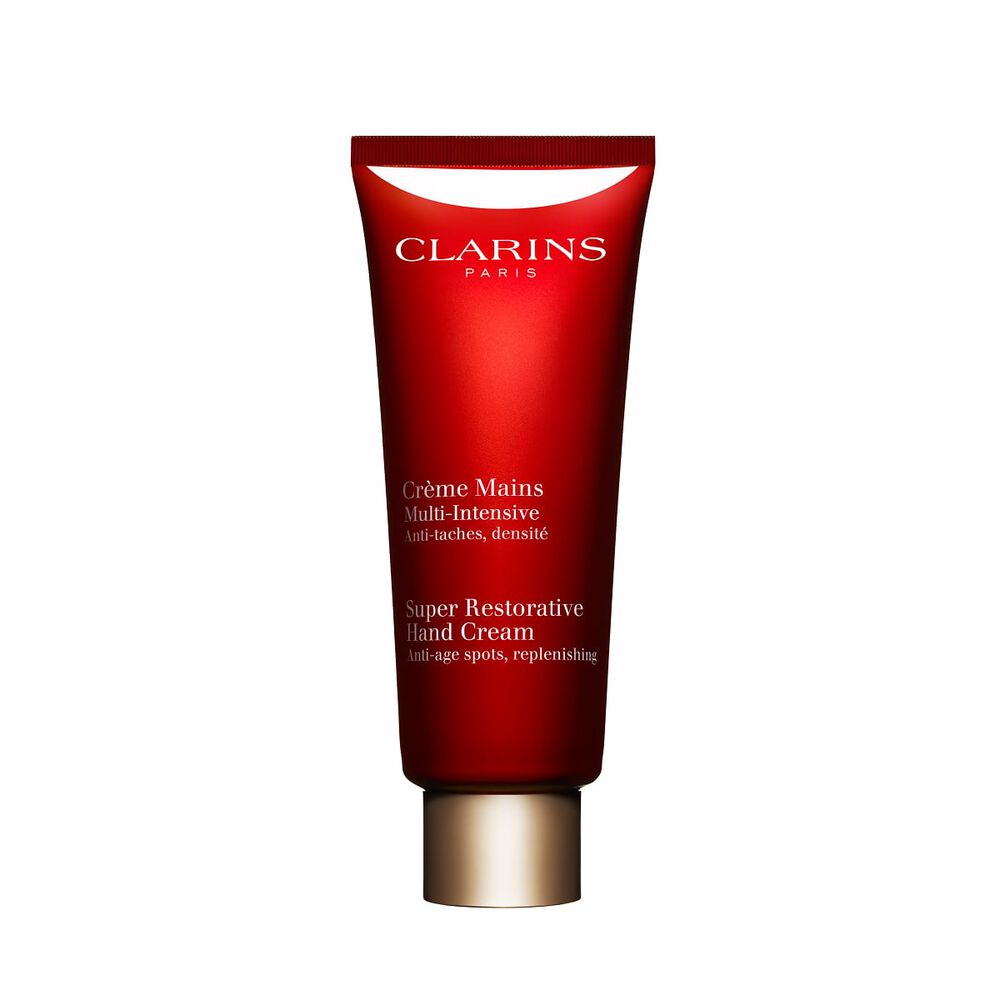 Packshot of a bottle of Clarins Super Restorative Hand Cream close to some harungana leaves on a pink background.