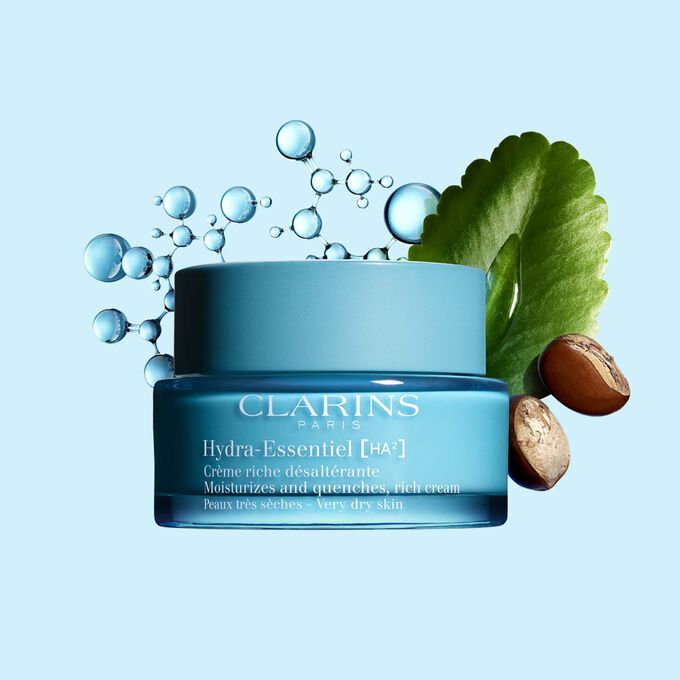 Packshot of Clarins Hydra-Essentiel Rich Cream close to some shea nuts and a kalanchoe leave on a blue background.