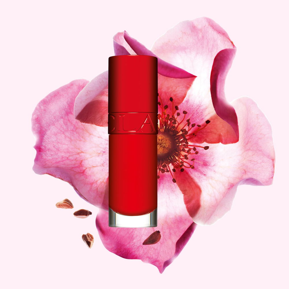 Packshot of Clarins Lip Comfort Oil in Iconic Red, placed next to a sweetbriar rose on a black-red background.