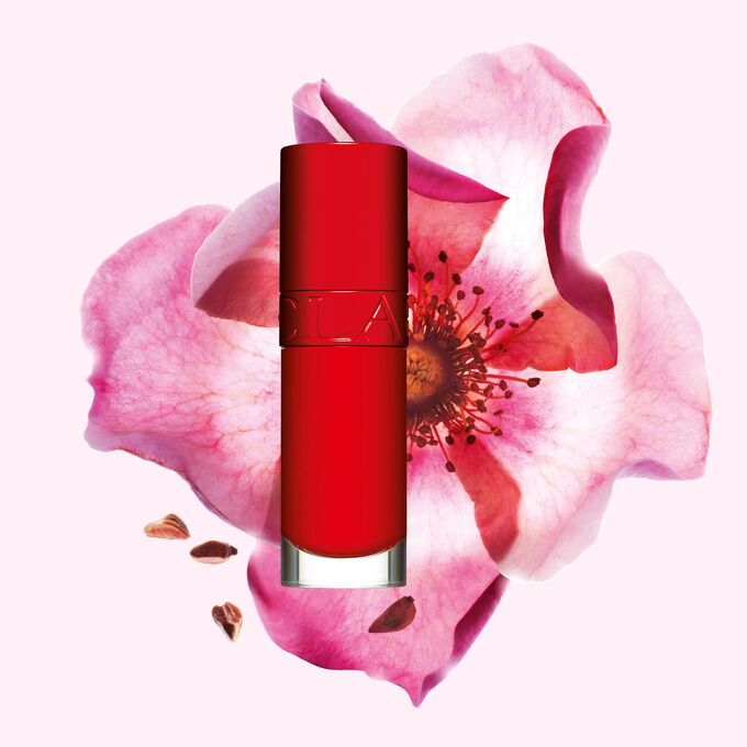 Packshot of Clarins Lip Comfort Oil in Iconic Red, placed next to a sweetbriar rose on a black-red background.