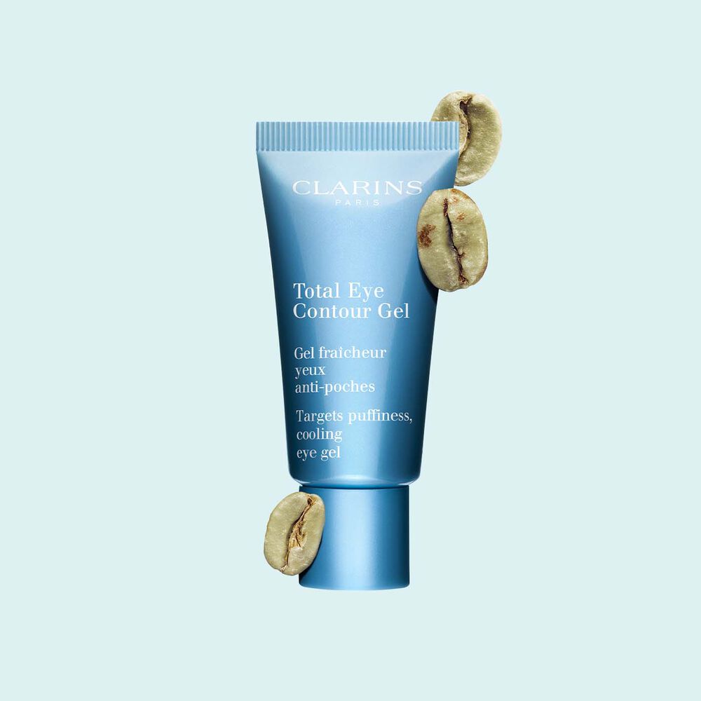 A tube of the Total Eye Contour Gel by Clarins close to coffee seeds on a blue background.