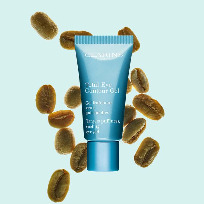 A tube of the Total Eye Contour Gel by Clarins close to coffee seeds on a blue background.