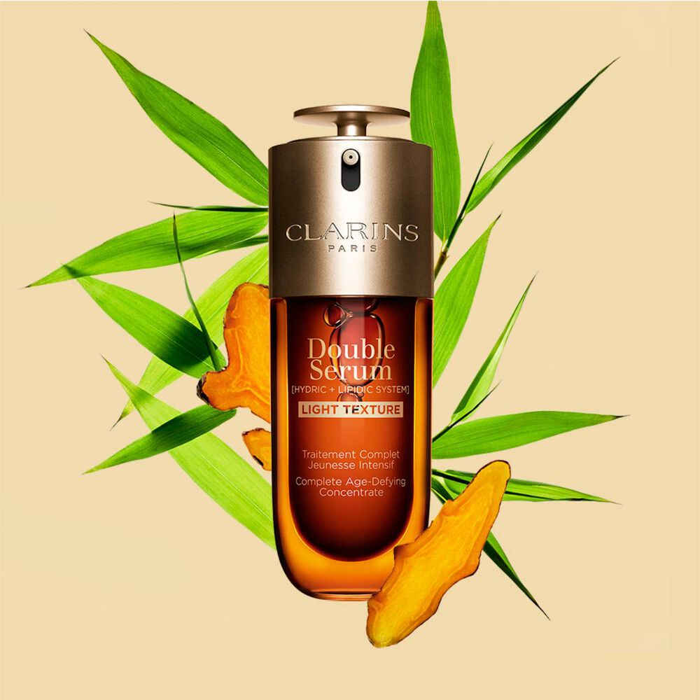 A 50 ml bottle of Clarins Double Serum Light Texture among turmeric and Provençal reed leaves against an orange background.