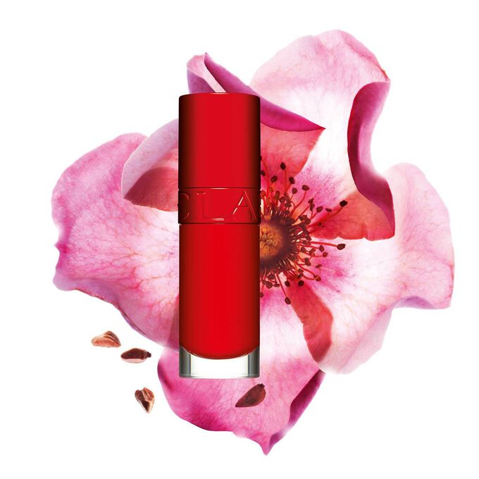 Packshot of Clarins Lip Comfort Oil in Iconic Red, placed next to a sweetbriar rose on a black-red background.