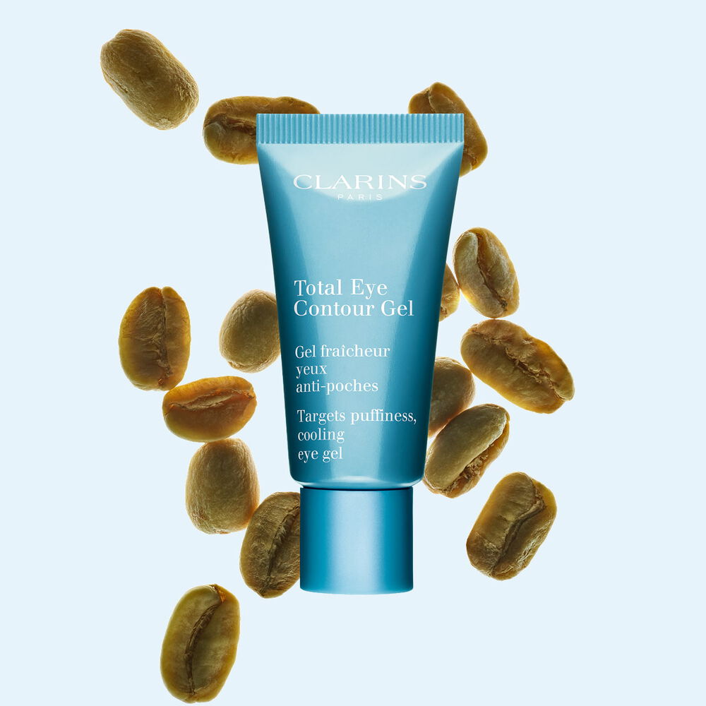 A tube of the Total Eye Contour Gel by Clarins close to coffee seeds on a blue background.
