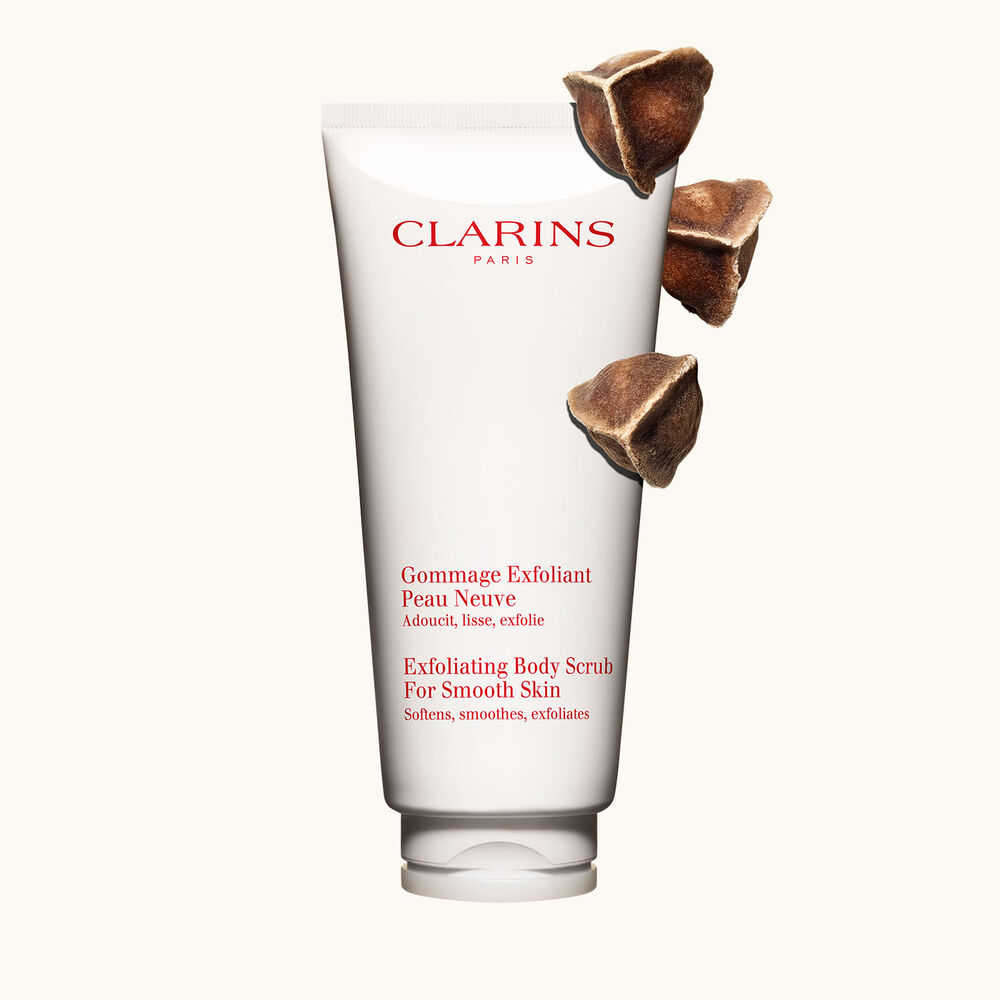 Packshot of Clarins Exfoliating Body Scrub for Smooth Skin placed next to moringa nuts on a light beige background.