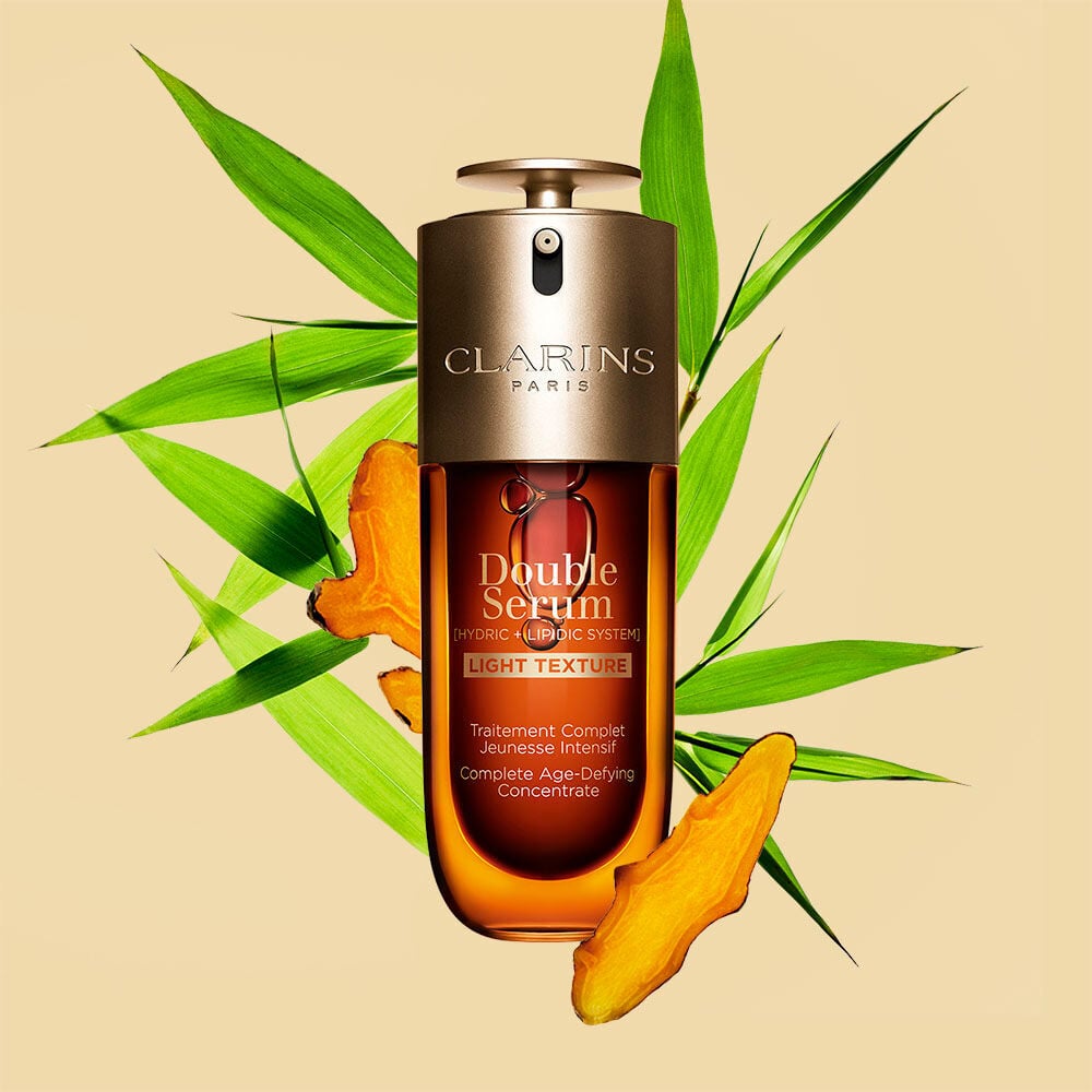 A 70 ml bottle of Clarins Double Serum Light Texture among turmeric and Provençal reed leaves against an orange background.