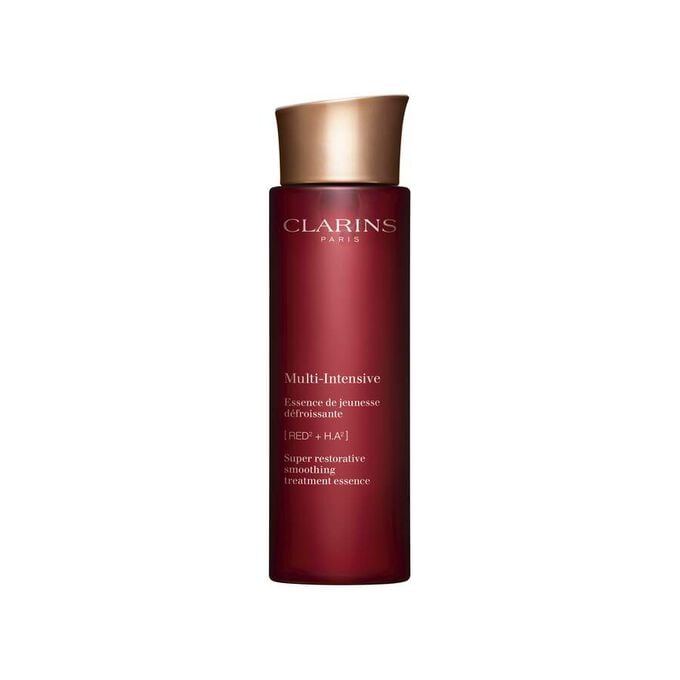 Packshot of Clarins Super Restorative Treatment Essence near red jania, Harungana leaves, and ginseng root on pink backdrop.