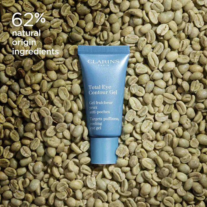 Tube of Clarins Total Eye Contour Gel among coffee seeds to illustrate the natural origin of the product's ingredients.