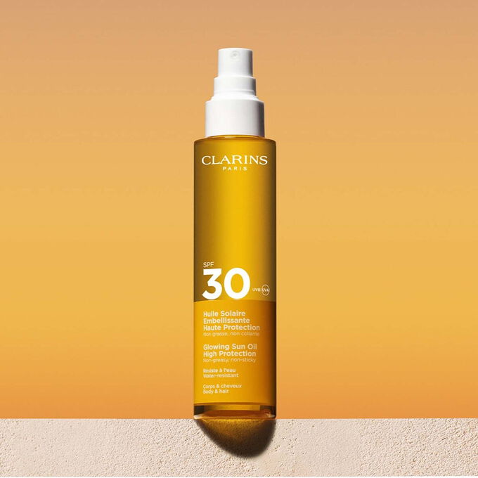 Packshot of a hair & body sun oil 30 spray with a message announcing that Clarins is committed to environmental protection