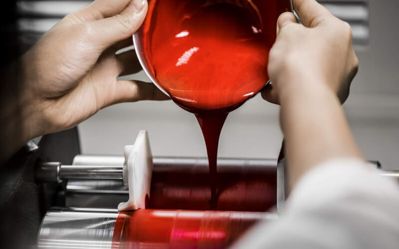 A technician pours a creamy preparation of red make-up into a machine