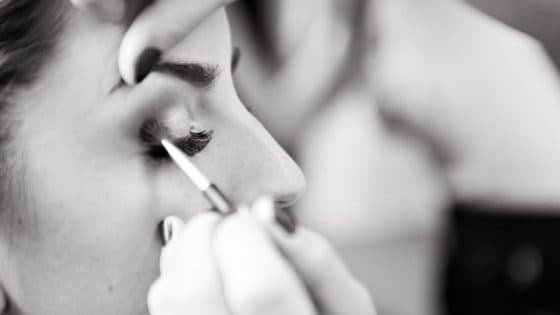 A black and white image of a woman having eyeshadow applied to her eyelid A black and white image of a woman having eyeshadow applied to her eyelid